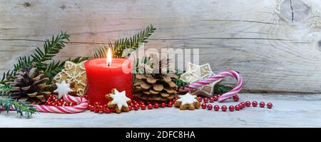 Rote brennende Kerze und Weihnachtsdekoration auf kaltgrauen Holzplanken, Panorama-Bannerformat, Kopierraum, ausgewählter Fokus, enge Schärfentiefe Stockfoto