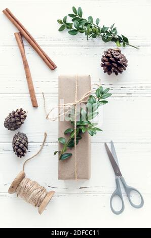 Prozess der Verpackung moderne Weihnachtsgeschenke mit natürlichen Dekorationen auf weißem Hintergrund. Geschenke Boxen in Handwerk Papier mit Garn und grüne Zweige. Stockfoto