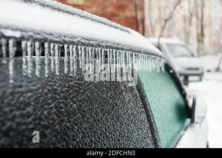 Eisbedecktes Autofenster aus der Nähe. Weißes Auto bedeckt mit Eis und Eiszapfen nach eisigen Regen. Schlechtes Winterwetter, Eissturm. Stockfoto