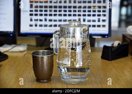 Eine Nahaufnahme einer Kupfertasse mit einem Glaskrug Gefüllt mit Wasser auf einer hölzernen Oberfläche Stockfoto