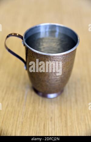 Eine Nahaufnahme eines Kupferbechers, der mit Wasser gefüllt ist Eine hölzerne Oberfläche Stockfoto