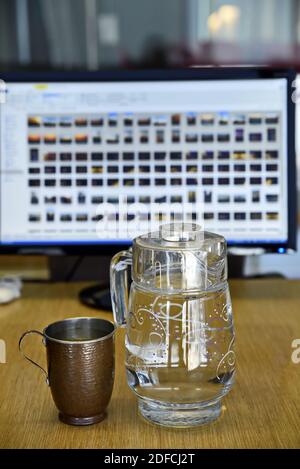 Eine Nahaufnahme einer Kupfertasse mit einem Glaskrug Gefüllt mit Wasser auf einer hölzernen Oberfläche Stockfoto