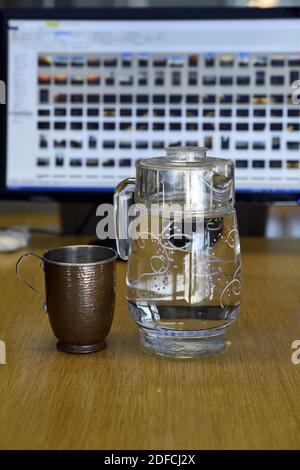 Eine Nahaufnahme einer Kupfertasse mit einem Glaskrug Gefüllt mit Wasser auf einer hölzernen Oberfläche Stockfoto