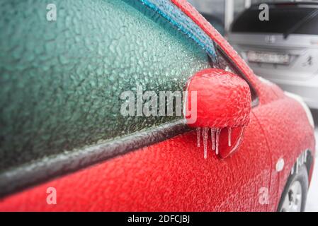 Eisbedecktes Autofenster aus der Nähe. Rotes Auto bedeckt mit Eis und Eiszapfen nach eisigen Regen. Schlechtes Winterwetter, Eissturm. Stockfoto