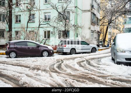 Spuren von den Rädern von Autos auf einer nassen verschneiten Straße. Auto bedeckt mit Eis, Schnee und Eiszapfen. Eissturmzyklon. Frostige Szenen im Winter. Stockfoto