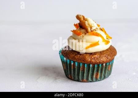 Eine einzelne Muffins in einem blauen Halter mit Glasur und Karottenrasur auf weißem Hintergrund, horizontal Stockfoto