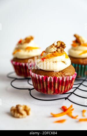 Drei Karottenkuchenmuffins in rosa und blau mit Glasur Und Karotten Rasieren auf Kühlregal weißen Hintergrund Stockfoto