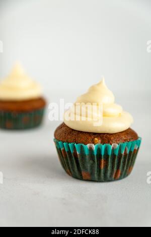 Zwei Muffins in blauem Halter mit Vereisung und Karotte Rasieren auf weißem Hintergrund Stockfoto
