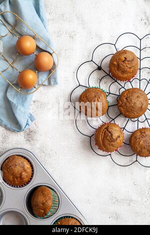 Muffins auf einem schwarzen Kühlregal mit Eiern in einem Korb und ein Backblech mit gebackenen Muffins Stockfoto