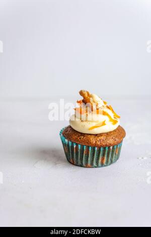Eine einzelne Muffins in einem blauen Halter mit Glasur und Karottenrasur auf weißem Hintergrund, vertikal Stockfoto