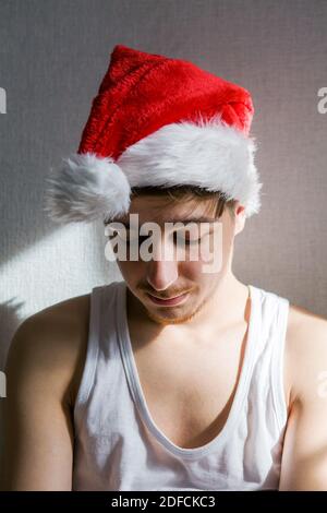 Trauriger junger Mann in Santa hat an der Wand in Das Zimmer Stockfoto
