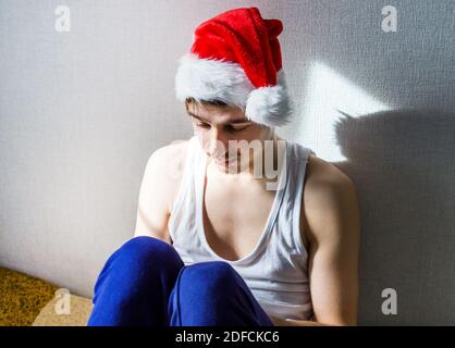 Trauriger junger Mann in Santa hat an der Wand in Das Zimmer Stockfoto