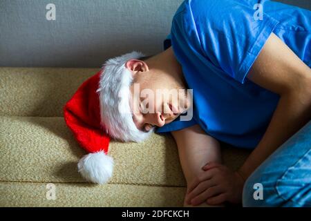 Junger Mann im Weihnachtsmütze schläft auf dem Sofa bei Das Zuhause Stockfoto