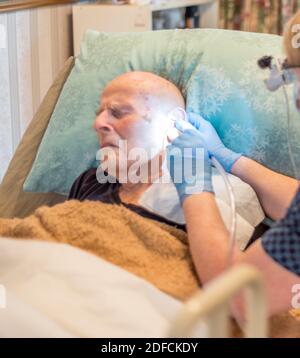 Bettlägiger älterer Mann, der sich lange einer unangenehmen, aber notwendigen Behandlung unterziehen muss Begriff Aufbau von Ohrenschmalz, verdichtet über die Ohrtrommel und Im Ohr Stockfoto