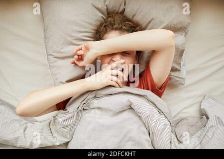 Blick auf die junge Frau, die in ihrem Bett liegt Und gähnend am Morgen aufwachen Stockfoto