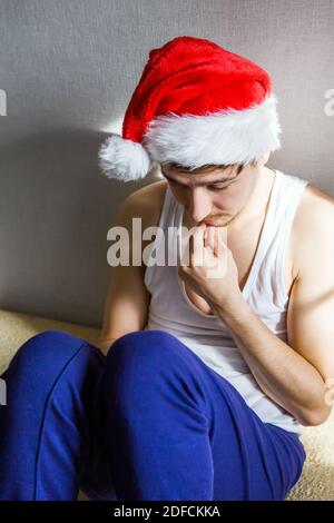 Trauriger junger Mann in Santa hat an der Wand in Das Zimmer Stockfoto