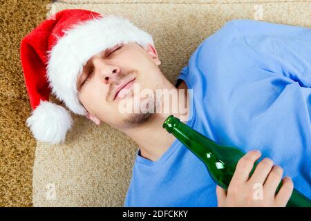 Ein Mann in Santa hat schlafen auf dem Sofa mit Ein Bier Stockfoto