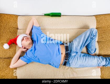 Ein Mann in Santa hat schlafen auf dem Sofa mit Ein Bier Stockfoto