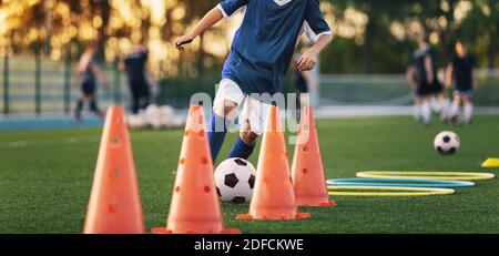 Fußball-Spieler auf Training Slalom Drill mit Ball. Soccer Boy läuft zwischen Red Training Kegel auf Gras Übungsfeld Stockfoto