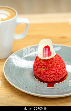 Luxus roten Dessert Shu Kuchen auf einem Teller mit einem tasse Latte auf dem Tisch in einem Café Stockfoto