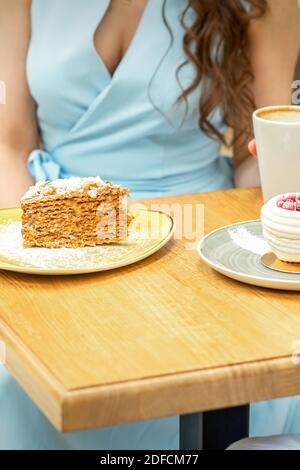Süße verschiedene Stücke Kuchen auf den Tellern am Tisch auf dem Hintergrund einer Frau mit einer Tasse Kaffee In einem Café Stockfoto