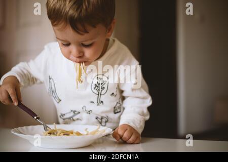 Netter kleiner Junge, der zu Hause Spaghetti isst Stockfoto