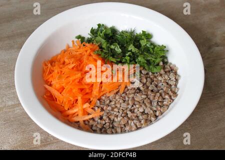 Buchweizenbrei mit geriebenen Karotten und Petersilie in weißem Teller auf Holztischuntergrund. Stockfoto