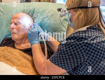 Bettlägiger älterer Mann, der sich lange einer unangenehmen, aber notwendigen Behandlung unterziehen muss Begriff Aufbau von Ohrenschmalz, verdichtet über die Ohrtrommel und Im Ohr Stockfoto