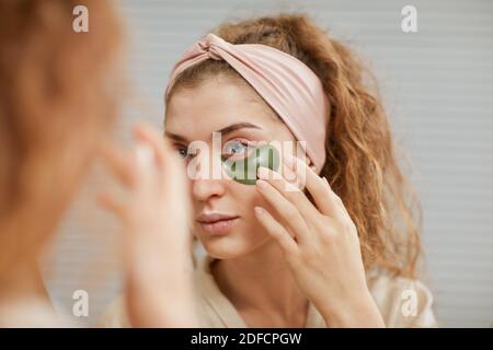 Junge Frau kümmert sich um ihr Gesicht Anwendung Flecken unter Ihre Augen schauten auf den Spiegel Stockfoto