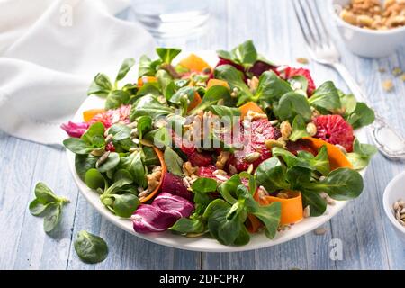 Grüner Salat mit Blutorangen, Karotten, Rüben, Samen und Nüssen auf hellblauem Hintergrund, freier Platz. Leckere gesunde Lebensmittel Stockfoto