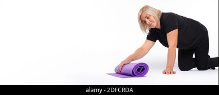 Banner. Ältere Frau faltet die Yogamatte zu Hause. Weißer Hintergrund. Platz. Stockfoto
