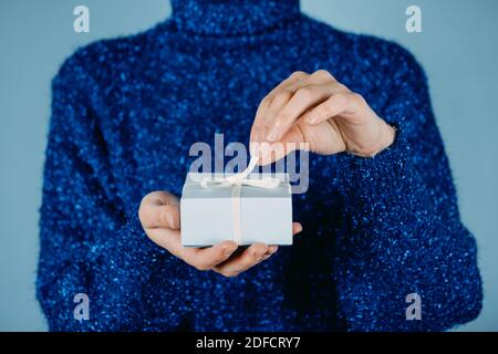 Frohe Weihnachtskarte, Hew Jahr, Weihnachten, Geburtstagsbanner. Weibliche Hände in blauen Pullover halten Handwerk Geschenkbox mit Band auf blauem Hintergrund. Stockfoto