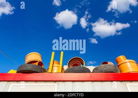 Die untere Ansicht ist auf Autoreifen und orangefarbenen Kunststoffrohren auf dem roten Metalldach des Containers, blauer wolkiger Himmel darüber. Stockfoto