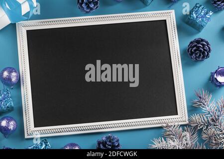 Fotorahmen mit freiem schwarzen Raum um Weihnachtsdekorationen und Geschenke auf blauem Hintergrund. Draufsicht, freier Platz für Text Stockfoto