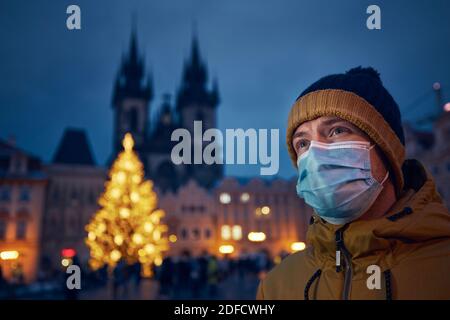Junger Mann mit Gesichtsmaske gegen Weihnachtsbaum in Prag. Themen Coronavirus-Pandemie während der Weihnachtsfeiertage und persönliche Verantwortung. Stockfoto