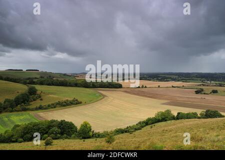 Heftiger Regen beginnt in dicken Laken am fernen Horizont zu fallen, während graue Wolken den Himmel füllen. Die grüne Wiltshire-Landschaft rollt in die Ferne. Stockfoto