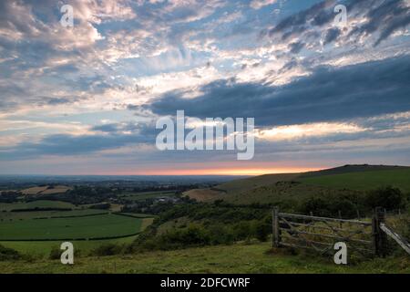 Der Horizont leuchtet mit warmen orangen Farben, als die Sonne beginnt, in der Ferne über die hügelige Landschaft von Dorset unter einem Himmel voller Wolken untergehen. Stockfoto