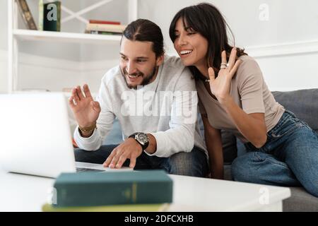 Bild von niedlichen fröhlichen Paar mit Laptop und winkende Hände Während Sie zu Hause auf dem Sofa sitzen Stockfoto