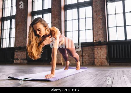 Junge langhaarige Frau tun Komplex von Stretching Yoga Asanas im Loft-Stil sonnigen Klasse mit ihrem Smartphone. Online-Unterricht und Training Stockfoto