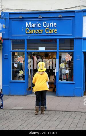 Ayr, Ayrshire, Schottland, Vereinigtes Königreich . Frau in gelb mit großem gelben Hut auf vor Marie Curie Cancer Care Shop Straße stehen Stockfoto