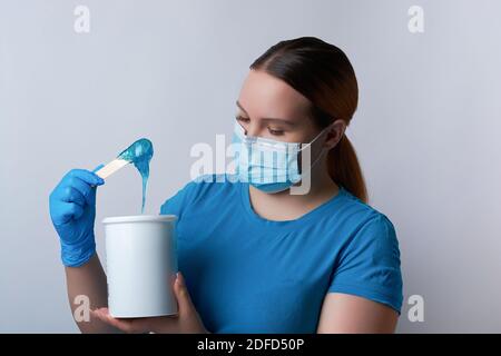 Ein Zuckermeister in blauen Handschuhen und einer medizinischen Maske hält einen Stock aus blauem Zuckerwachs. Enthaarung und Schönheitskonzept Stockfoto