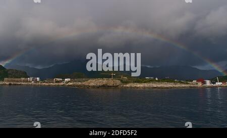 Schöner mehrfarbiger Regenbogen an der Küste der Insel Austvågøya, Lofoten, Norwegen in der Nähe des Dorfes Svolvaer mit traditionellen hölzernen Trockenregalen. Stockfoto