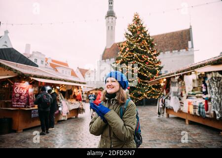 Tallinn, Estland. Junge Schöne Hübsche Kaukasische Mädchen Frau In Grüne Jacke Und Blauen Hut Gekleidet Genießen Leben Und Lächeln Auf Hintergrund Weihnachten Stockfoto