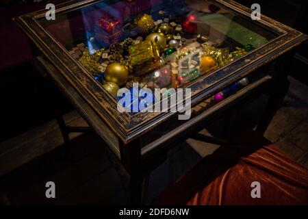 Vintage Holztisch mit goldenen Weihnachtskugeln, blau eingewickelten Weihnachtsgeschenken und Mahjong Holzwürfel unter Glas-Tischplatte. Innenausstattung für den Urlaub Stockfoto