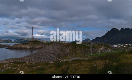 Felsküste im Süden des Fischerdorfes Henningsvær, Insel Austvågøya, Lofoten, Norwegen mit Fußballplatz, Holztrocknungsständer für Stockfisch. Stockfoto