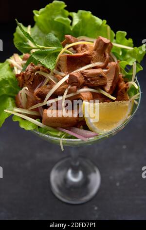 Eingelegte Pfifferlinge Pilze, mit Kräutern und Salat, in einer Glasschale, auf schwarzem Hintergrund Stockfoto