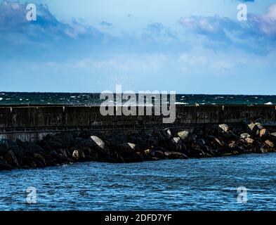 Wellen, die in einem Sturm auf einen Wellenbrechersteg stürzen und Wasser über den Pier schicken. Stockfoto