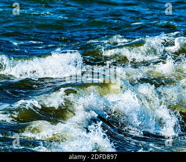 Brüllende Wellen mit Schaum, die im Sturm auf Felsen auf einem Wellenbrecherpier krachen. Stockfoto