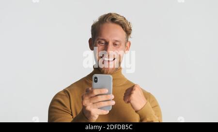 Schöner bärtiger Mann glücklich über gute Geschäft mit Smartphone Für Arbeiten isoliert auf weißem Hintergrund Stockfoto
