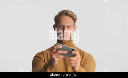 Junge attraktive bärtige Mann spielt im Spiel auf Smartphone über weißem Hintergrund. Moderne Technik Stockfoto